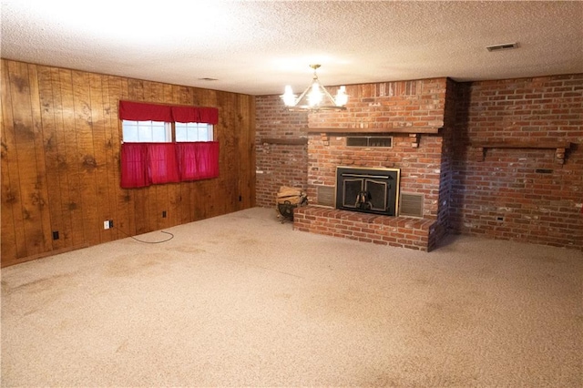 unfurnished living room featuring a fireplace, a textured ceiling, a chandelier, wood walls, and carpet