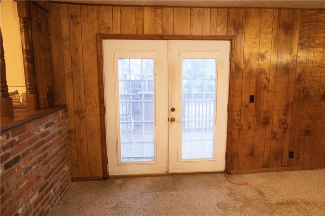 entryway with wood walls, light colored carpet, and french doors