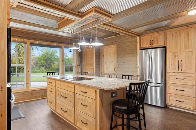 kitchen featuring black electric stovetop, a kitchen island with sink, dark wood-type flooring, stainless steel refrigerator, and wood walls