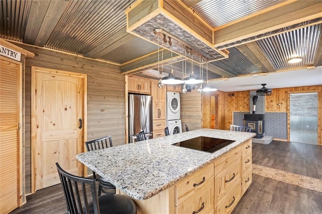 kitchen featuring stainless steel fridge, stacked washing maching and dryer, wooden walls, a wood stove, and a center island