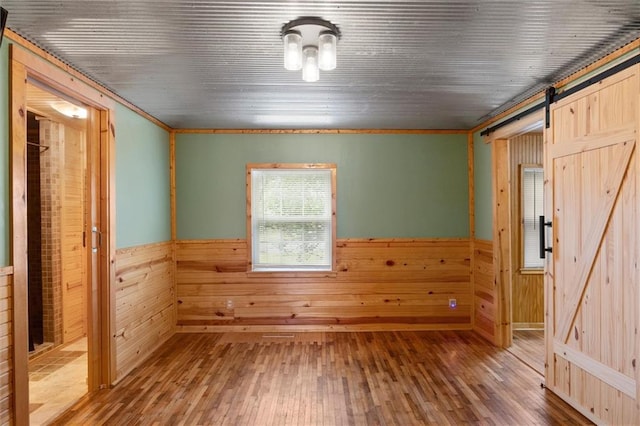 spare room with crown molding, hardwood / wood-style floors, a barn door, and wooden walls