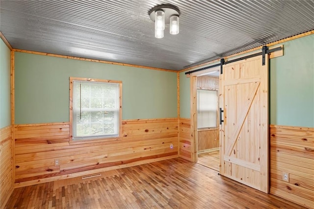 spare room with crown molding, a barn door, hardwood / wood-style flooring, and wood walls