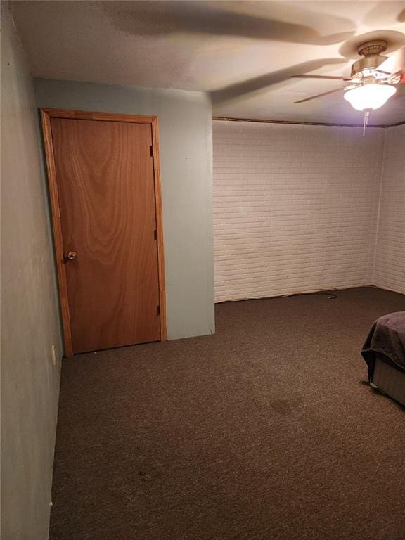 spare room with brick wall, dark colored carpet, and ceiling fan