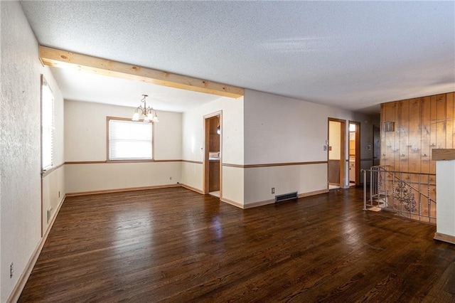 unfurnished room featuring beam ceiling, a chandelier, dark wood-type flooring, and a textured ceiling