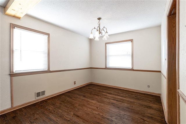 empty room with a textured ceiling, plenty of natural light, dark wood-type flooring, and a chandelier