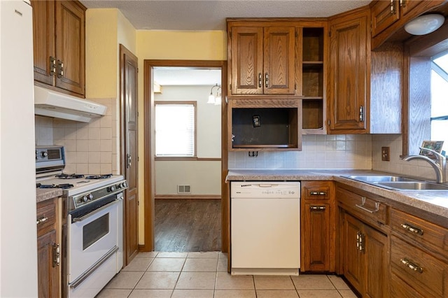 kitchen featuring backsplash, sink, light tile patterned flooring, and white appliances