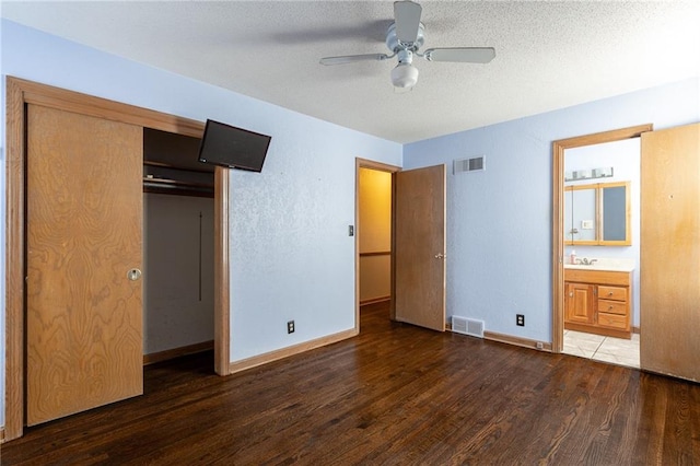 unfurnished bedroom with dark hardwood / wood-style flooring, ensuite bathroom, a textured ceiling, ceiling fan, and a closet