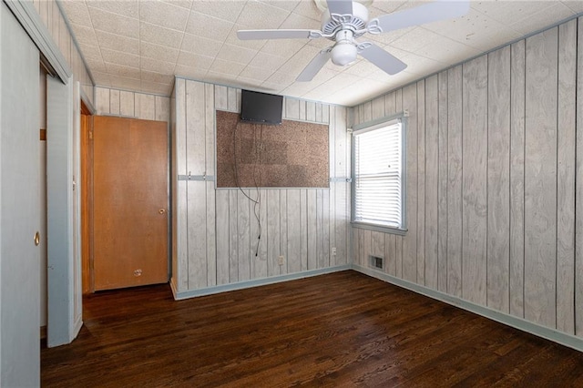 unfurnished room with ceiling fan, dark wood-type flooring, and wood walls