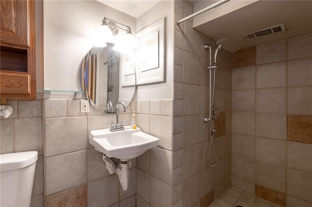 bathroom with a tile shower, tile walls, and toilet