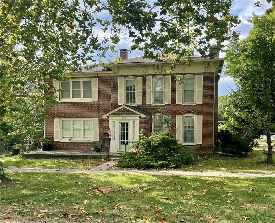 view of front facade featuring a front yard, brick siding, and a chimney