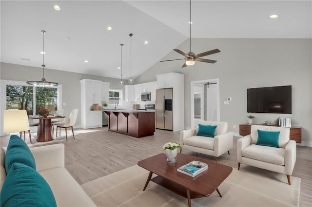 living room featuring high vaulted ceiling, light hardwood / wood-style floors, ceiling fan, and a barn door