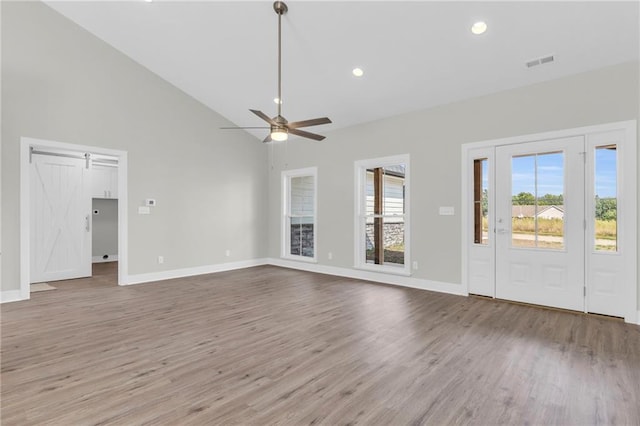 unfurnished living room featuring high vaulted ceiling, wood-type flooring, ceiling fan, and a barn door