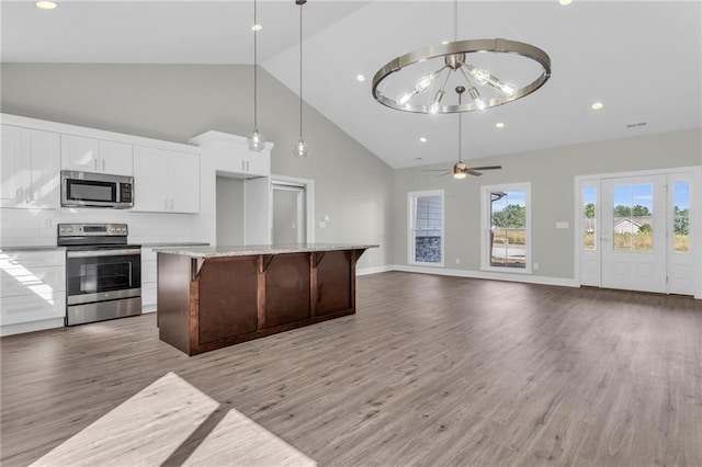 kitchen featuring white cabinetry, a kitchen bar, hanging light fixtures, a kitchen island, and appliances with stainless steel finishes