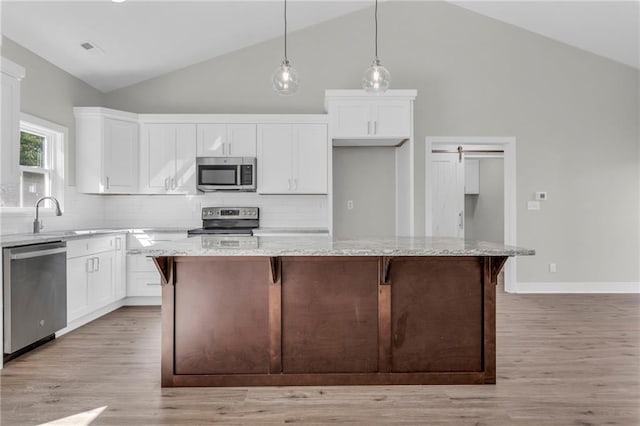 kitchen featuring a kitchen island, light stone countertops, stainless steel appliances, and white cabinetry