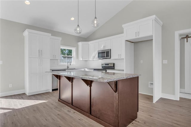 kitchen with white cabinetry, vaulted ceiling, a kitchen island, stainless steel appliances, and light stone countertops