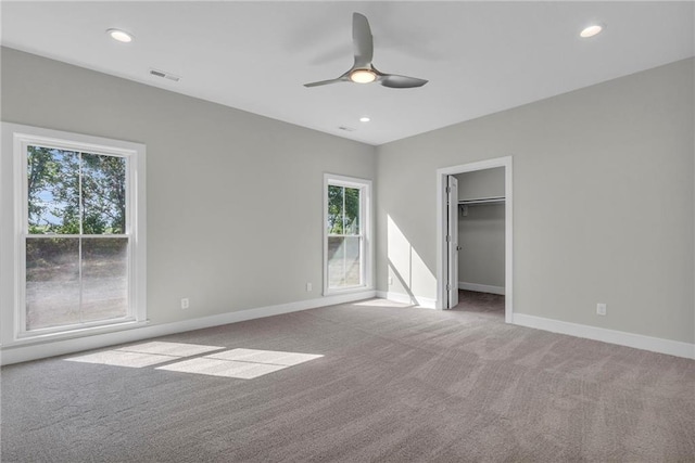 unfurnished bedroom with a spacious closet, multiple windows, light colored carpet, and ceiling fan