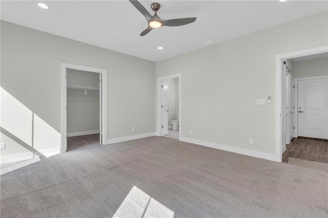 unfurnished bedroom with a closet, light colored carpet, ensuite bathroom, a spacious closet, and ceiling fan