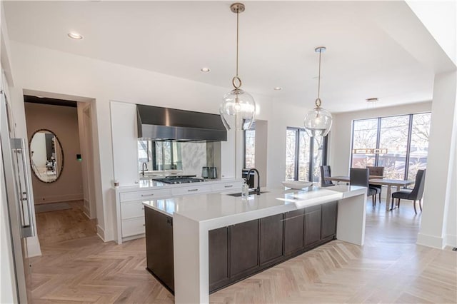 kitchen featuring a kitchen island with sink, light parquet flooring, white cabinetry, sink, and wall chimney exhaust hood