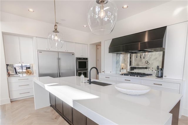 kitchen featuring pendant lighting, stainless steel appliances, sink, white cabinets, and wall chimney range hood