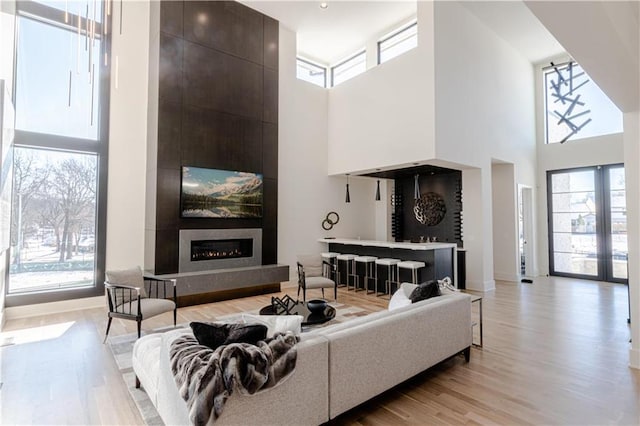 living room with a high ceiling, a large fireplace, light wood-type flooring, and a healthy amount of sunlight