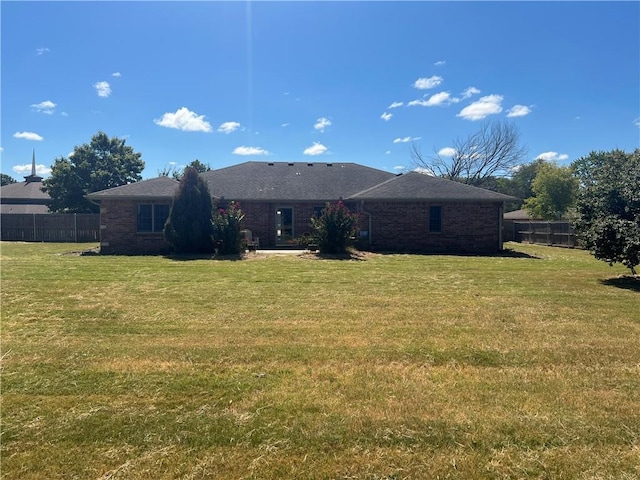 rear view of house featuring fence, brick siding, and a yard