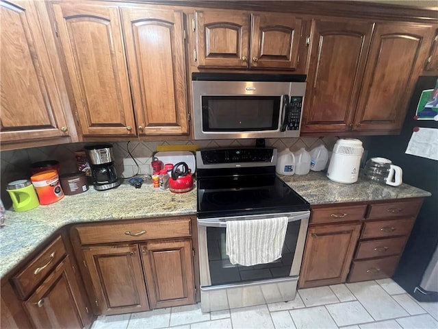 kitchen featuring decorative backsplash, stainless steel appliances, brown cabinetry, and light stone counters