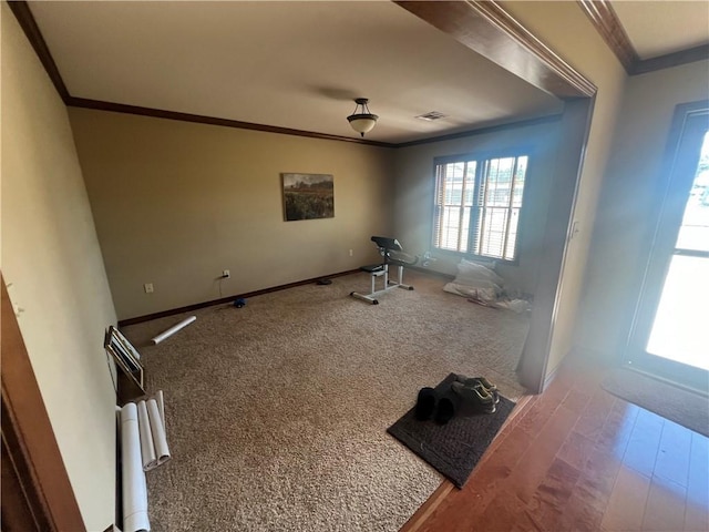 interior space with carpet flooring, visible vents, crown molding, baseboards, and wood finished floors