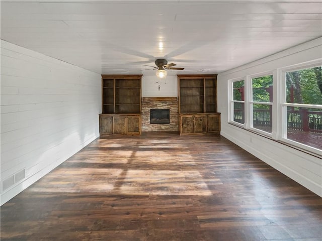 unfurnished living room with a stone fireplace, dark hardwood / wood-style floors, and ceiling fan