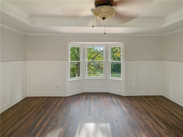 unfurnished room with a tray ceiling, dark wood-type flooring, and crown molding