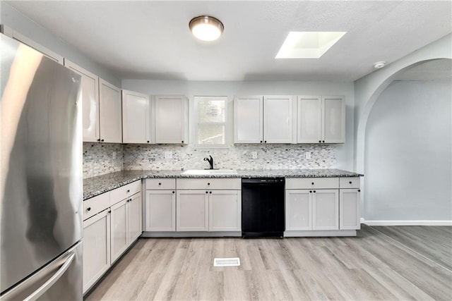 kitchen with dishwasher, sink, white cabinetry, stainless steel refrigerator, and a skylight