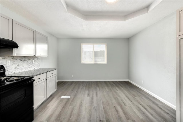 kitchen with a raised ceiling, black electric range oven, backsplash, white cabinetry, and light wood-type flooring