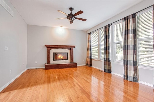 unfurnished living room featuring ceiling fan, a premium fireplace, and light wood-type flooring