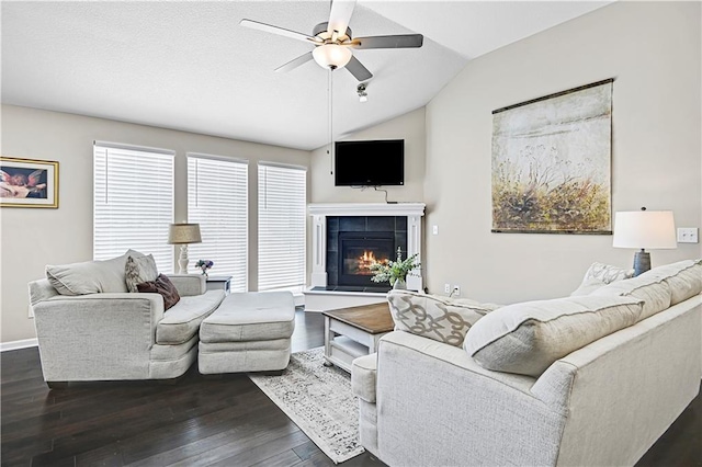 living room with lofted ceiling, ceiling fan, a tile fireplace, dark wood-style flooring, and baseboards