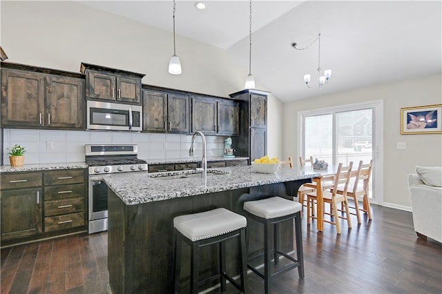 kitchen featuring appliances with stainless steel finishes, hanging light fixtures, an island with sink, and dark brown cabinets