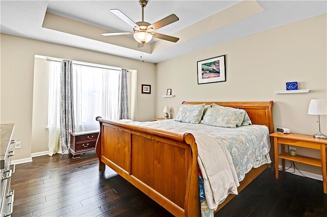 bedroom with dark wood-style flooring, a raised ceiling, a ceiling fan, and baseboards