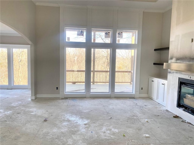 unfurnished living room featuring baseboards, a high ceiling, ornamental molding, and a glass covered fireplace