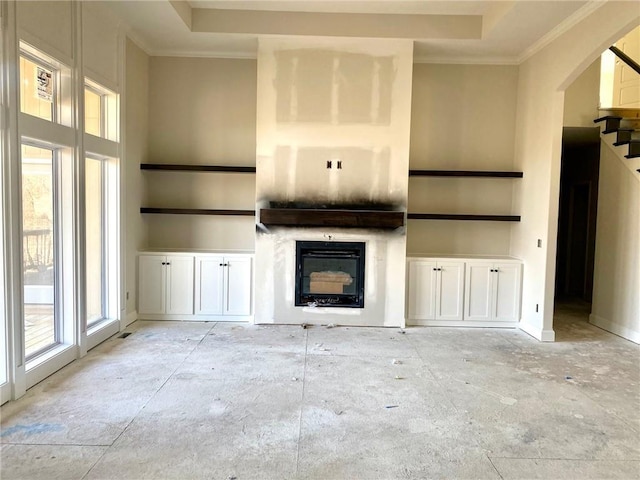 unfurnished living room featuring stairs, ornamental molding, a raised ceiling, and a glass covered fireplace