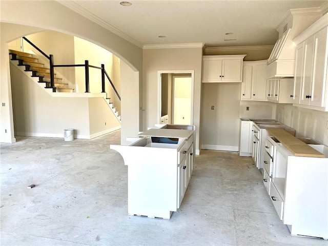 kitchen featuring arched walkways, white cabinetry, custom exhaust hood, a center island, and unfinished concrete flooring