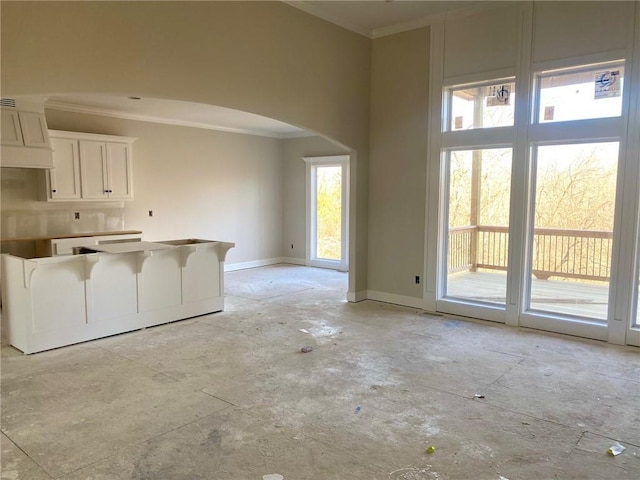 unfurnished living room with baseboards, arched walkways, and ornamental molding