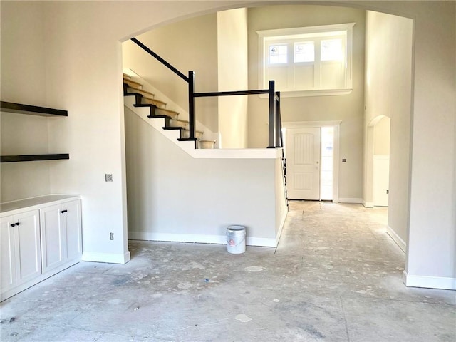 entryway featuring arched walkways, concrete flooring, a high ceiling, baseboards, and stairway