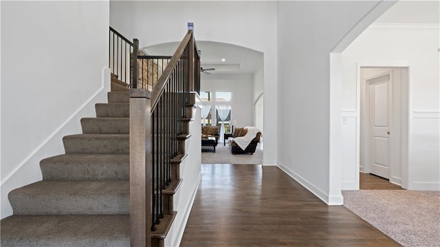 stairs featuring a ceiling fan, arched walkways, baseboards, and wood finished floors