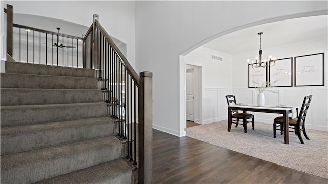 stairway with arched walkways, a decorative wall, wood finished floors, visible vents, and an inviting chandelier