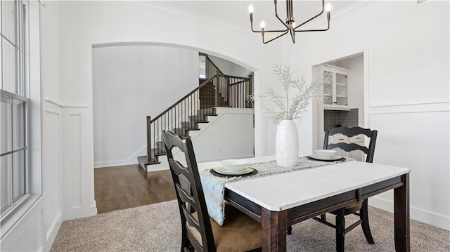 dining area featuring arched walkways, crown molding, a decorative wall, an inviting chandelier, and stairs