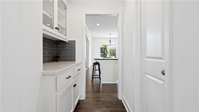 hall featuring dark wood-style floors, an inviting chandelier, a sink, and baseboards