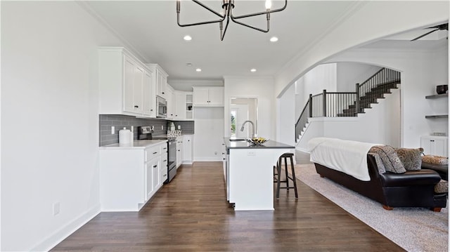 kitchen with arched walkways, appliances with stainless steel finishes, open floor plan, dark wood-style flooring, and ornamental molding