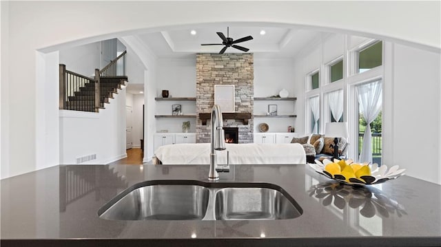 kitchen featuring visible vents, ceiling fan, a tray ceiling, a fireplace, and a sink