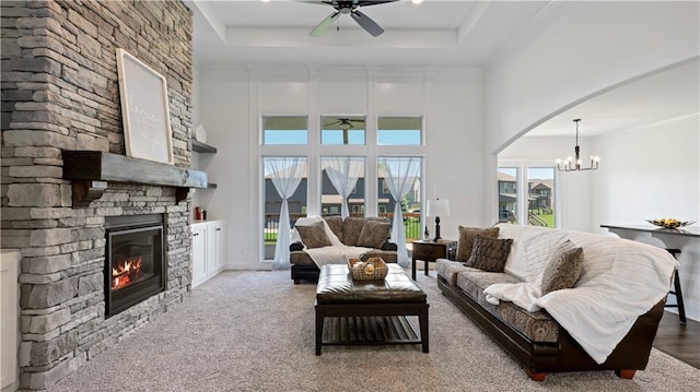 living room featuring arched walkways, a high ceiling, a tray ceiling, a fireplace, and ceiling fan with notable chandelier