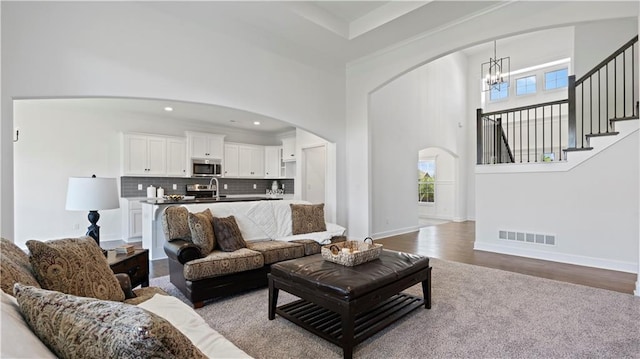 living room with arched walkways, visible vents, stairway, a high ceiling, and an inviting chandelier