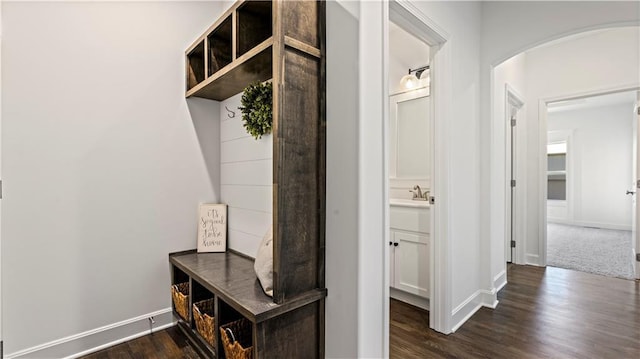 mudroom featuring dark wood-style floors, arched walkways, a sink, and baseboards