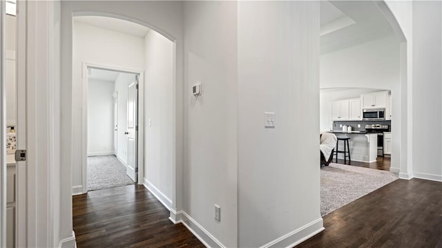 hallway with arched walkways, dark wood-style flooring, a high ceiling, and baseboards